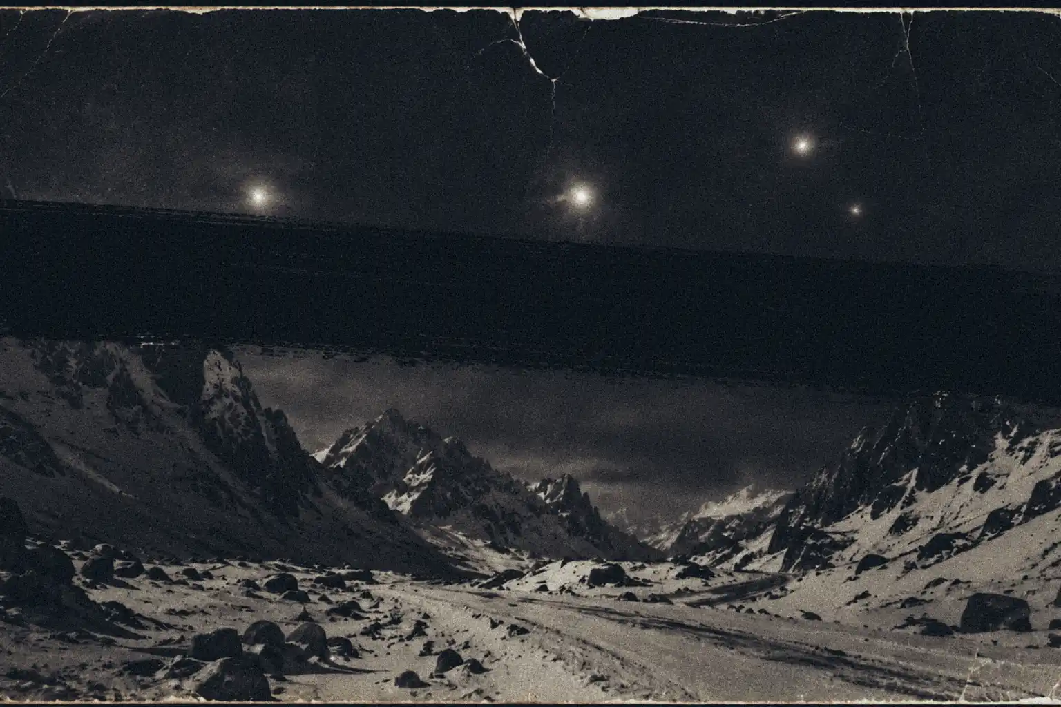A crinkled 1959 black-and-white photograph showing faint glowing spheres over a snow-covered mountain pass at night. A thick, black redaction marker stroke is slashed across the centre of the photo, obscuring the evidence.