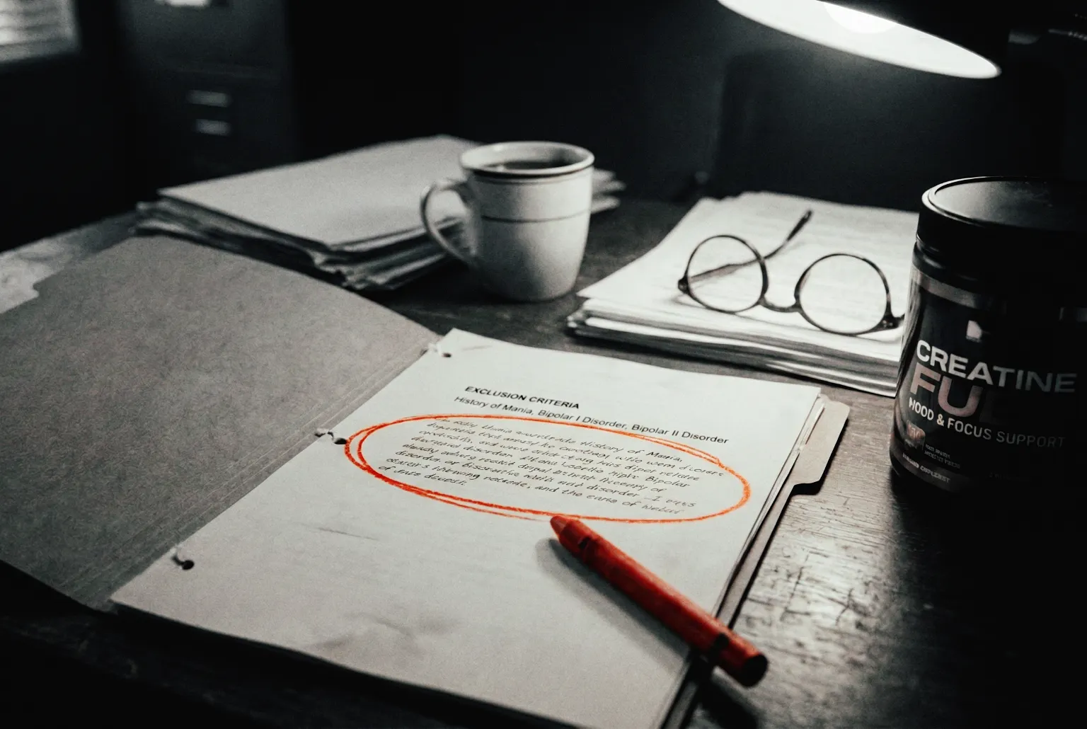 A forensic still life of an investigator's desk featuring a clinical trial protocol with the text 'Exclusion Criteria: History of Mania, Bipolar I Disorder' circled in red, placed next to a commercial tub of creatine supplement labeled 'Mood & Focus Support'.