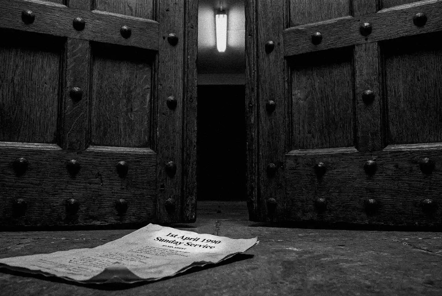 A low-angle, gritty photograph of the heavy wooden double doors to the HMP Manchester chapel